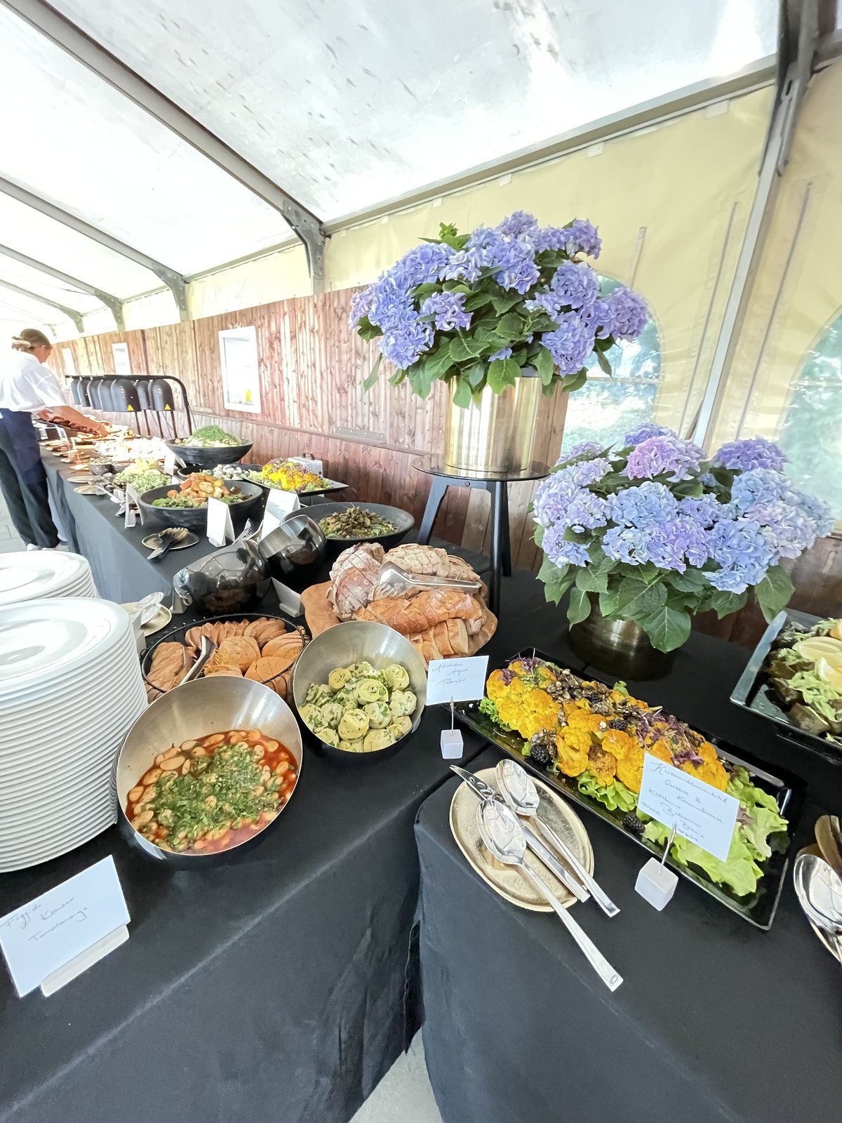 Hochwertig aufgebautes Buffet mit floralen Akzenten in einem hellen Veranstaltungszelt